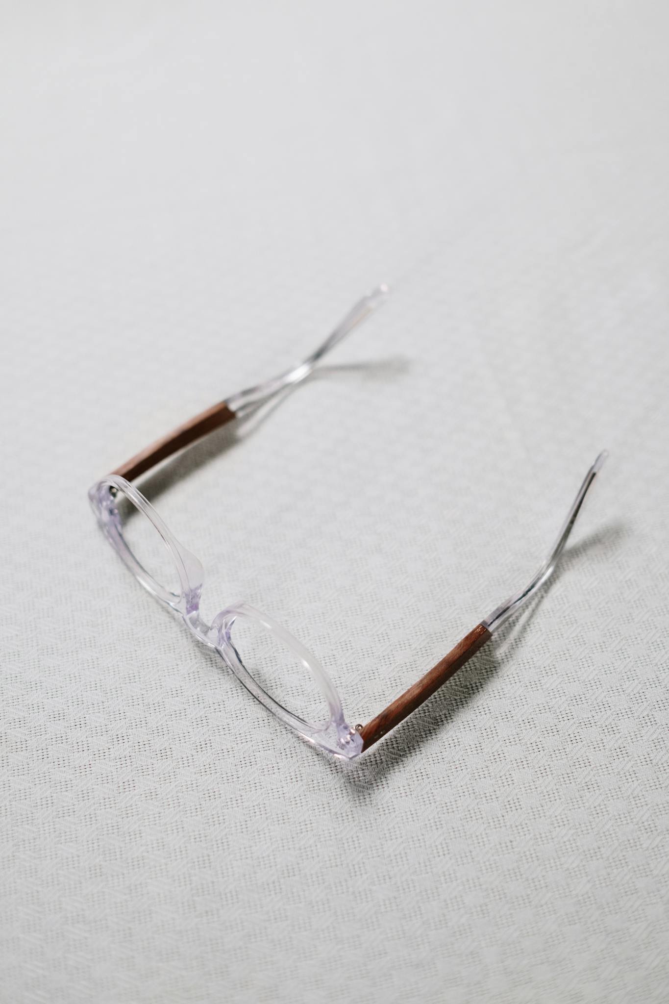 Close-up of clear eyeglasses with brown temples on a textured white surface.