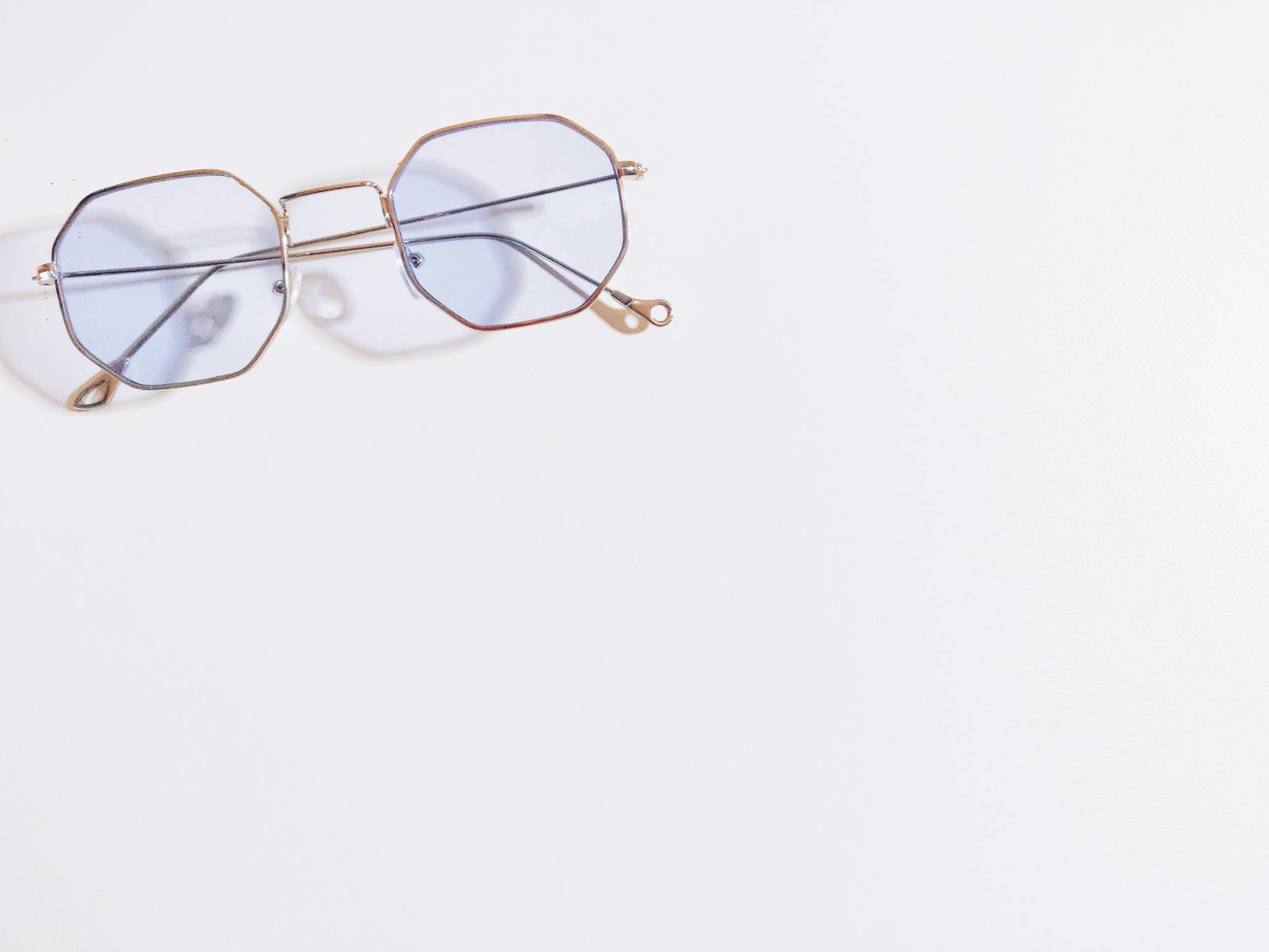 Close-up of hexagonal eyeglasses with blue tint on a white background, minimalistic style.