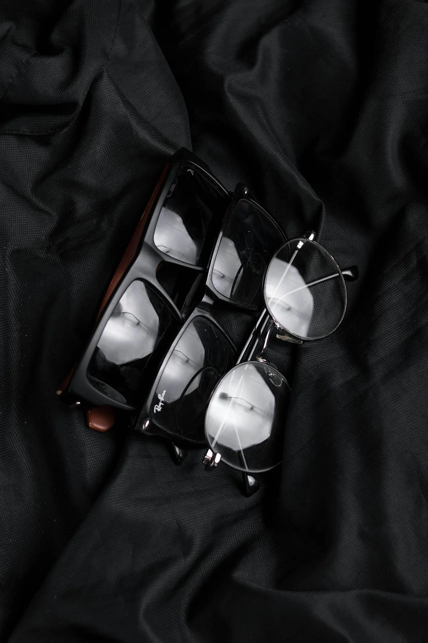 Close-up of various stylish eyeglasses on black fabric, highlighting modern eyewear design.