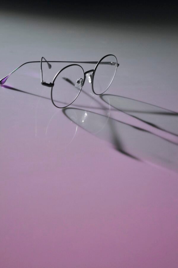 Round eyeglasses with metal frames casting shadows on a neon purple surface, emphasizing modern eyewear style.